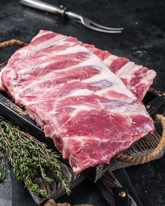 Raw pork belly on a dark surface with herbs and a fork.