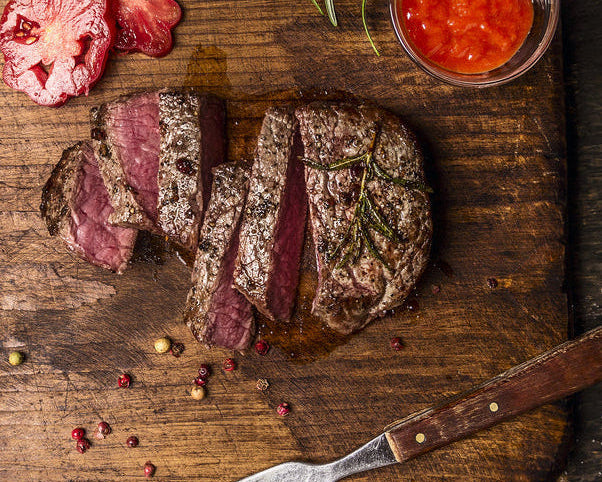 Sliced steak on a wooden cutting board with herbs and a knife