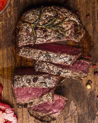 Sliced steak on a wooden cutting board with herbs and a knife