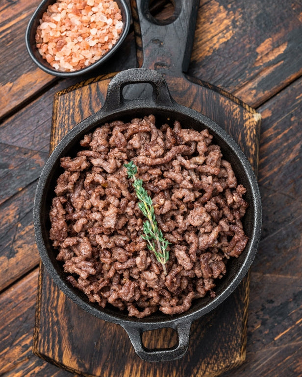 Sautéed ground meat with a sprig of rosemary in a cast iron skillet on a wooden surface.