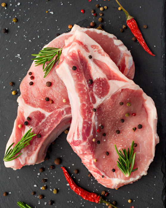 Raw pork meat steaks on a slate board with herbs and spices