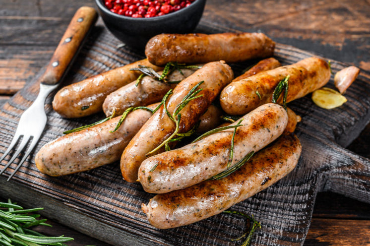 Grilled sausages on a wooden cutting board with rosemary and red pepper flakes.
