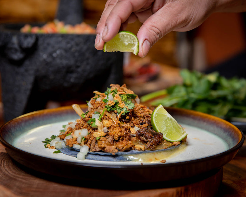 Person squeezing a lime wedge over a dish of pork ground dish on a wooden table.