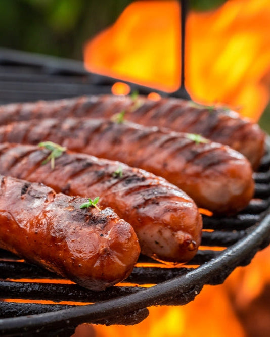 Grilled pork sausages on a barbecue grill with flames in the background