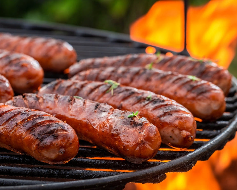 Grilled pork sausages on a barbecue grill with flames in the background