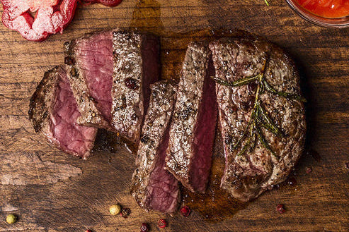 Sliced steak on a wooden cutting board with herbs and a knife