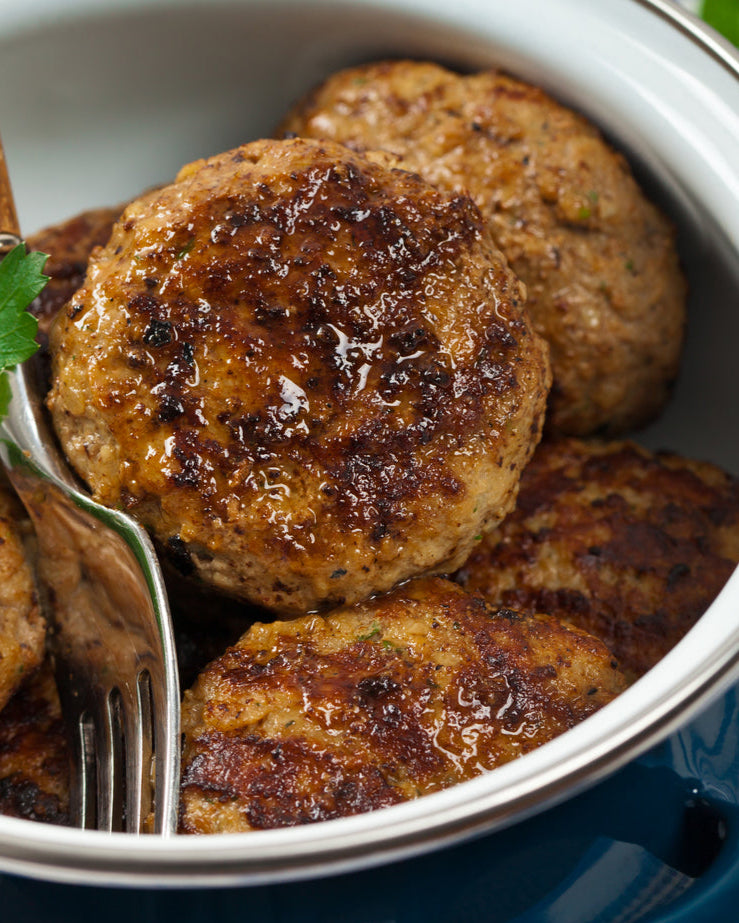 Bowl of browned pork meatballs with a fork on a blue and white patterned tablecloth.